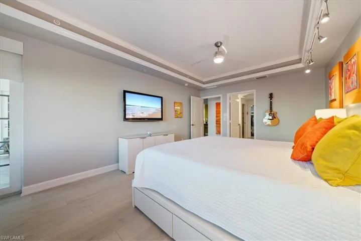 Bedroom with a tray ceiling, light wood finished floors, and ceiling fan