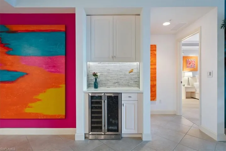 Indoor dry bar featuring white cabinetry, wine cooler, decorative backsplash, light tile patterned floors, and light stone counters