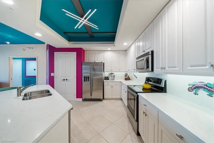 Kitchen with stainless steel appliances, recessed lighting, light stone counters, white cabinets, and a tray ceiling
