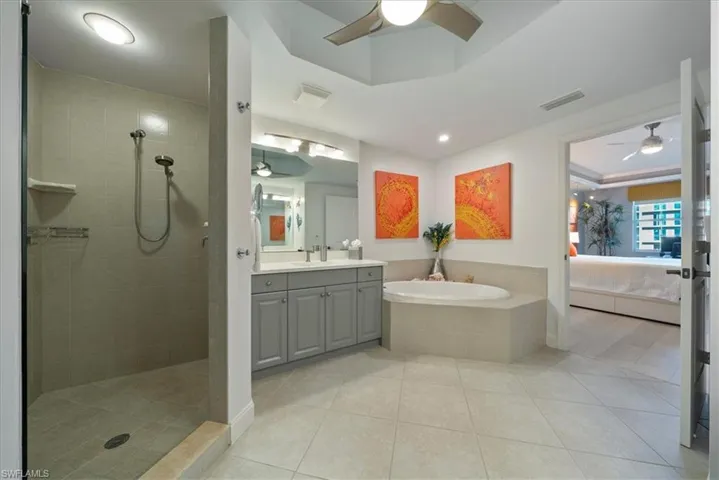 Ensuite bathroom featuring a ceiling fan, vanity, walk in shower, a tray ceiling, and a garden tub