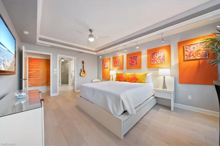 Bedroom featuring a raised ceiling, rail lighting, light wood-type flooring, a ceiling fan, and ensuite bath