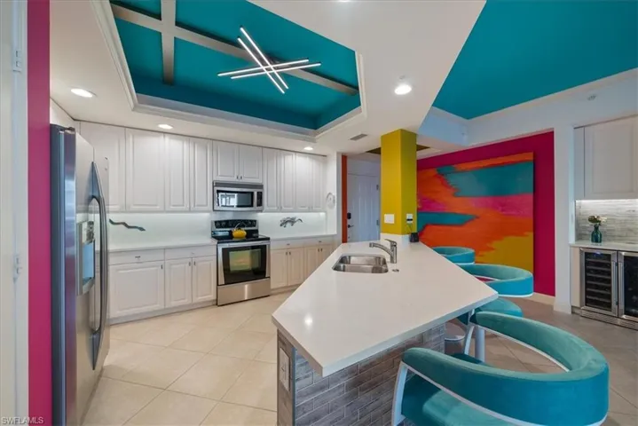 Kitchen featuring stainless steel appliances, beverage cooler, a kitchen bar, recessed lighting, and white cabinetry
