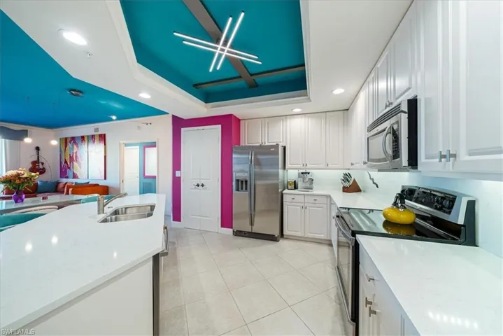 Kitchen featuring stainless steel appliances, recessed lighting, light stone countertops, white cabinets, and a tray ceiling