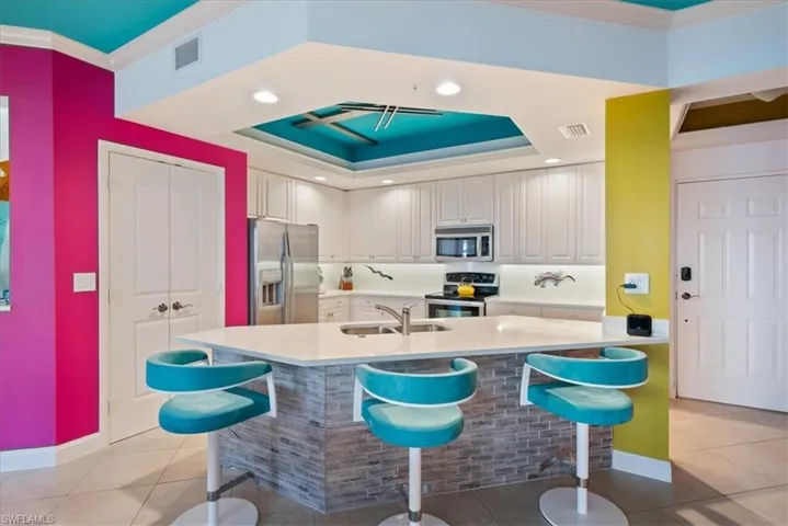 Kitchen featuring stainless steel appliances, a breakfast bar area, a raised ceiling, recessed lighting, and light tile patterned flooring