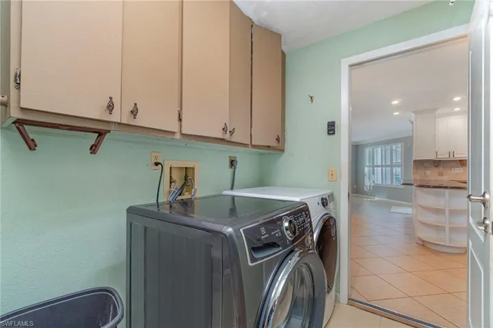 Washroom with cabinets, light tile patterned floors, and washer and clothes dryer