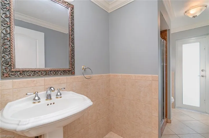 Bathroom with a shower with door, sink, ornamental molding, tile patterned floors, and tile walls