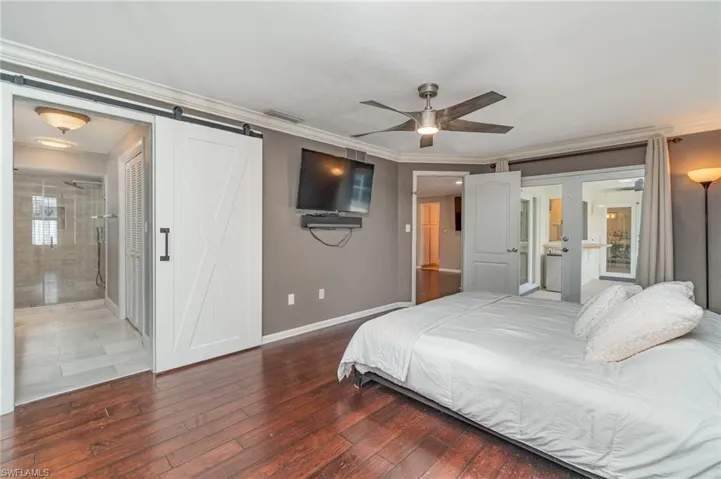 Bedroom with wood-type flooring, a barn door, connected bathroom, ornamental molding, and ceiling fan