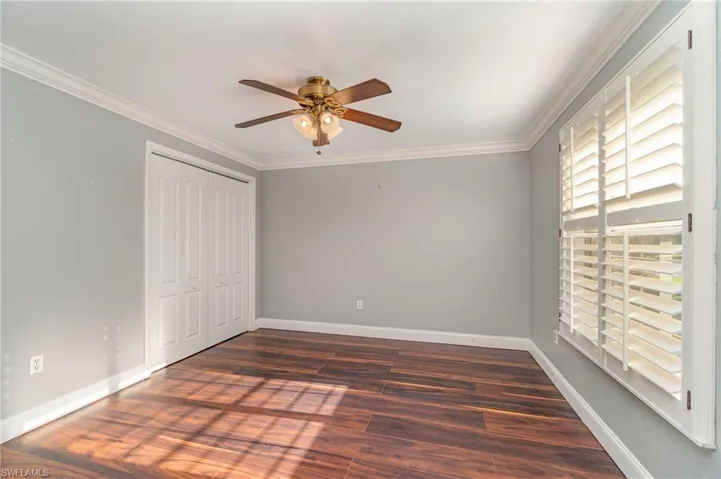 Unfurnished bedroom with dark hardwood / wood-style flooring, ceiling fan, crown molding, and a closet