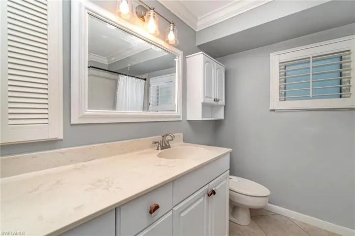 Bathroom with tile patterned floors, ornamental molding, walk in shower, vanity, and toilet