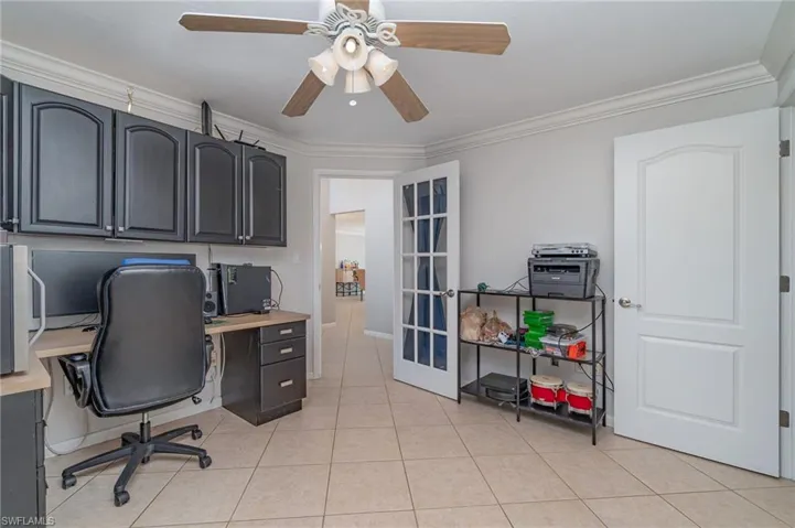 Office area with french doors, built in desk, ornamental molding, light tile patterned floors, and ceiling fan