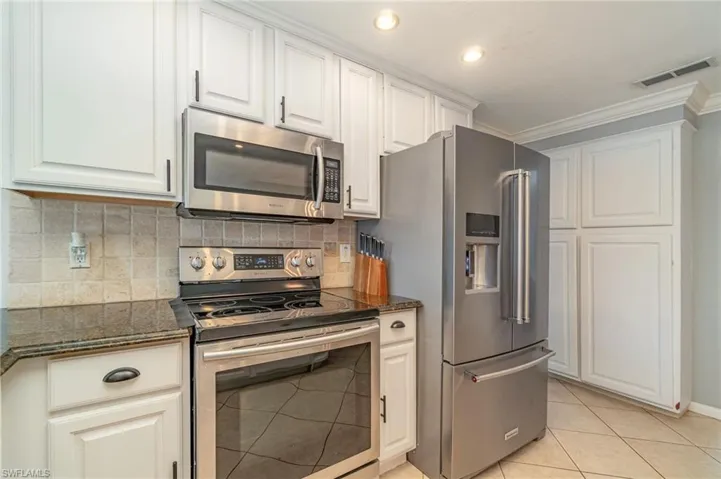 Kitchen with stainless steel appliances, light tile patterned floors, tasteful backsplash, ornamental molding, and white cabinetry