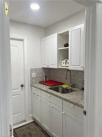 Kitchen featuring light stone counters, backsplash, sink, and white cabinets