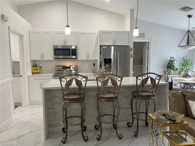 Kitchen featuring a kitchen island, vaulted ceiling, appliances with stainless steel finishes, and a breakfast bar area