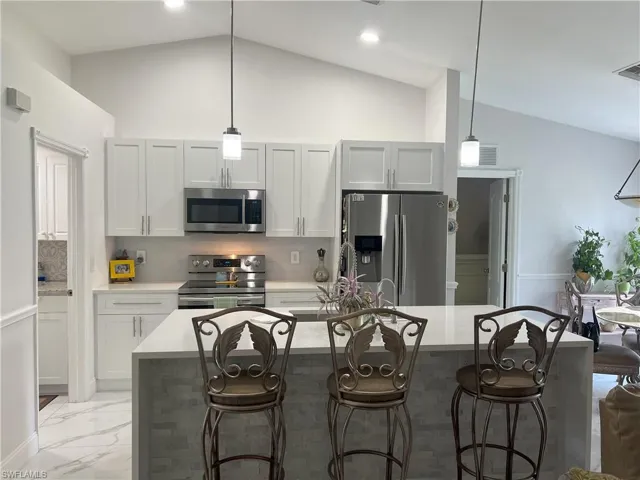 Kitchen with a kitchen island with sink, lofted ceiling, stainless steel appliances, and tasteful backsplash