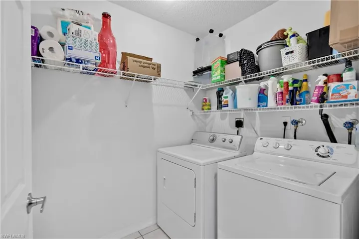 Laundry area with washer and dryer, a textured ceiling, and light tile patterned floors