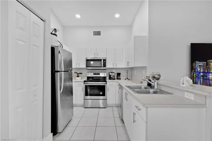 Kitchen with stainless steel appliances, white cabinetry, sink, kitchen peninsula, and light tile patterned flooring