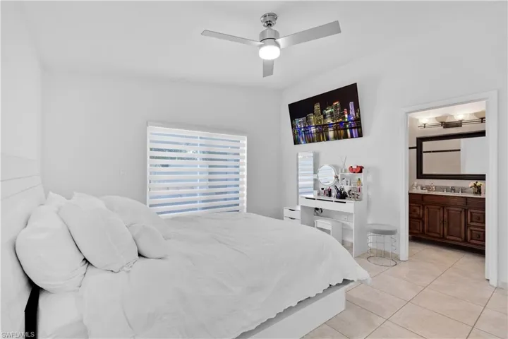 Bedroom with ceiling fan, connected bathroom, and light tile patterned floors