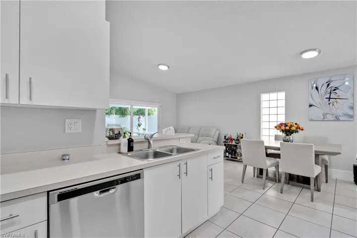 Kitchen featuring dishwasher, sink, lofted ceiling, white cabinets, and light tile patterned floors