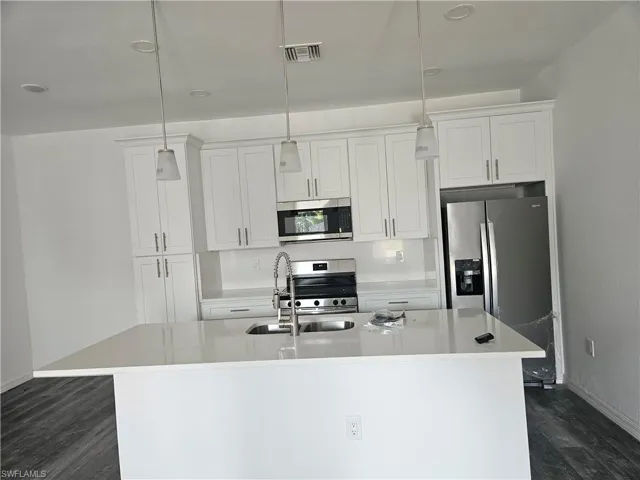 Kitchen with appliances with stainless steel finishes, a kitchen island with sink, dark wood-style flooring, and white cabinets