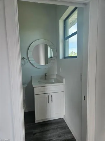 Half bath with baseboards, wood finished floors, toilet, and vanity