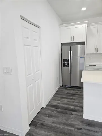 Kitchen with fridge, white cabinetry, light countertops, and dark wood-style flooring