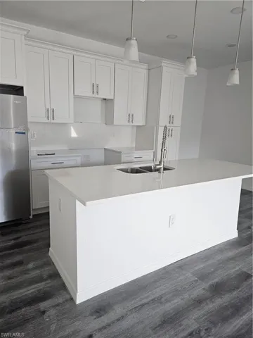 Kitchen with a sink, refrigerator, a center island with sink, white cabinets, and dark wood-style flooring