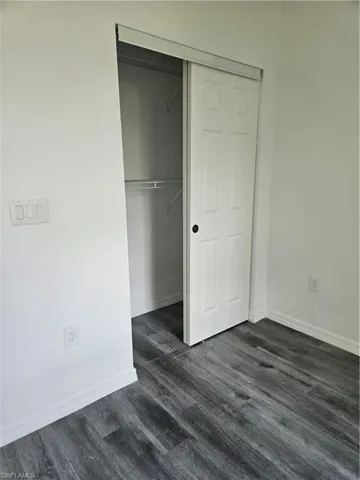 Unfurnished bedroom with a closet, dark wood-style flooring, and baseboards