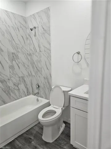 Bathroom with wood finished floors, toilet, vanity, and bathing tub / shower combination