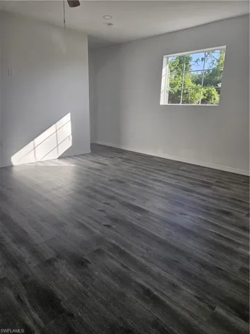 Spare room featuring baseboards, dark wood-style floors, and a ceiling fan