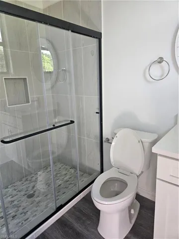 Bathroom featuring a stall shower, wood finished floors, toilet, and vanity