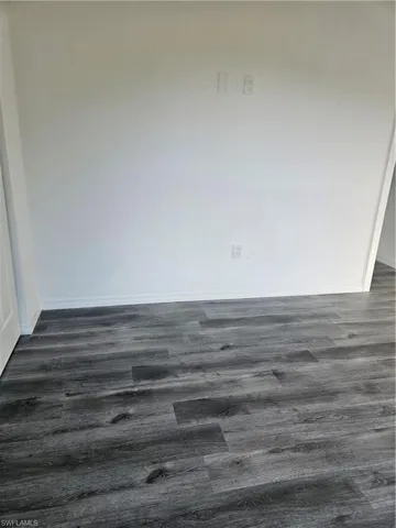 Spare room with dark wood-style floors and baseboards