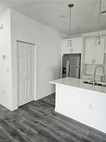Kitchen featuring white cabinets, light countertops, refrigerator, dark wood-type flooring, and a sink