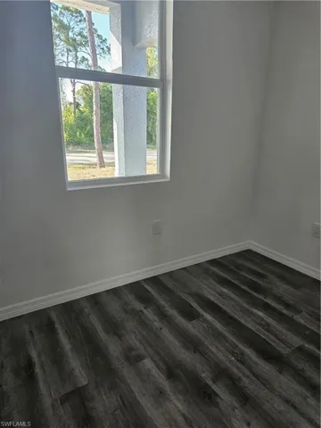 Spare room featuring baseboards and dark wood-style flooring