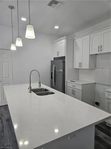 Kitchen featuring an island with sink, a sink, stainless steel fridge with ice dispenser, light stone countertops, and visible vents