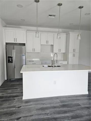 Kitchen with a kitchen island with sink, white cabinets, and refrigerator