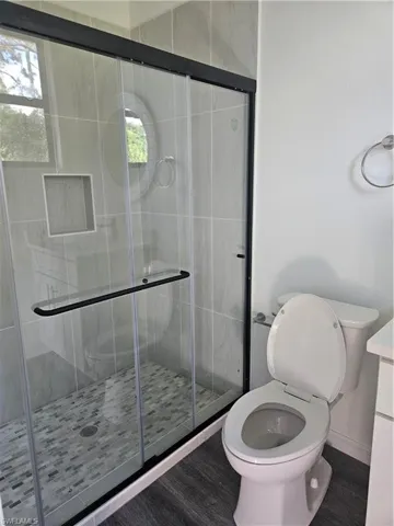 Full bath featuring wood finished floors, toilet, and a shower stall
