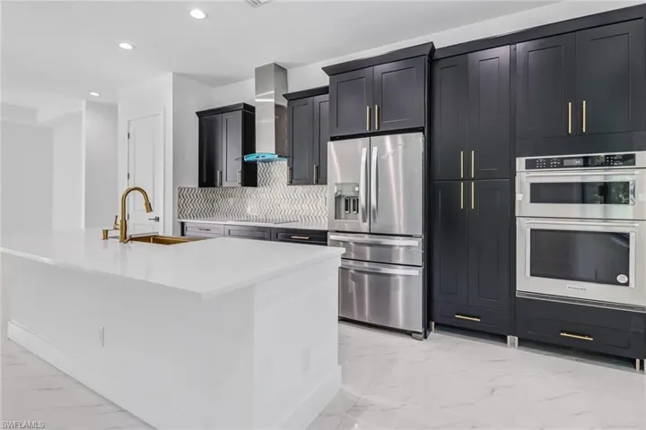 Kitchen featuring appliances with stainless steel finishes, a center island with sink, wall chimney range hood, sink, and backsplash
