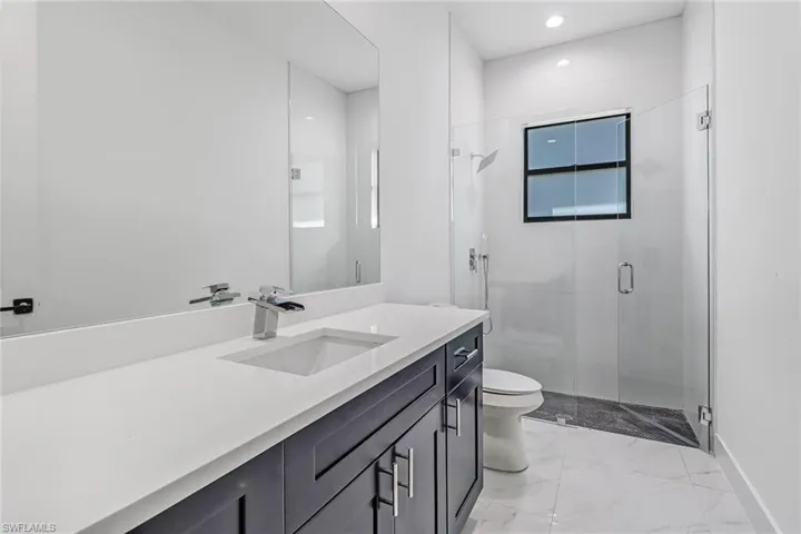 Bathroom with a shower with shower door, vanity, tile patterned floors, and toilet