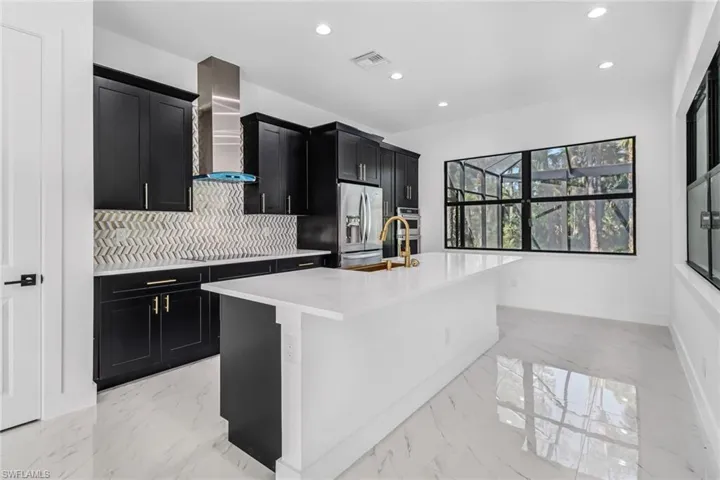 Kitchen with decorative backsplash, a center island with sink, wall chimney exhaust hood, and light tile patterned floors