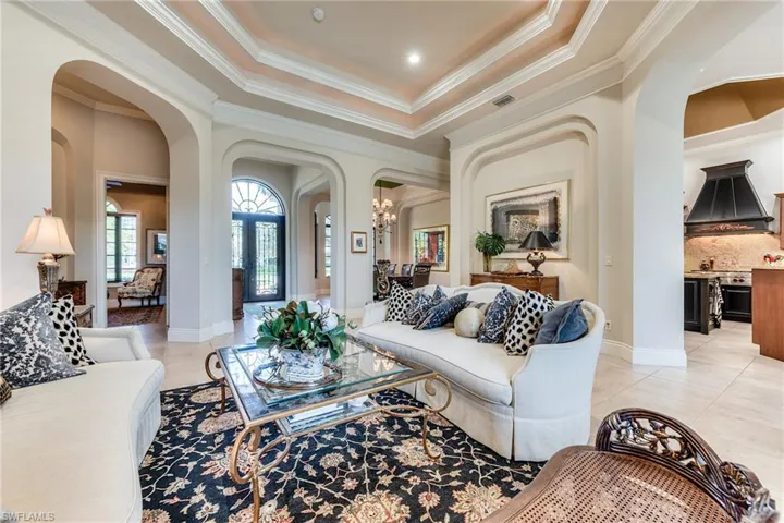 Living room with arched walkways, light tile patterned flooring, crown molding, visible vents, and an inviting chandelier