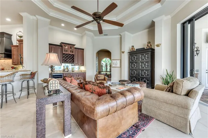 Living room featuring light tile patterned floors, arched walkways, a raised ceiling, and ornamental molding