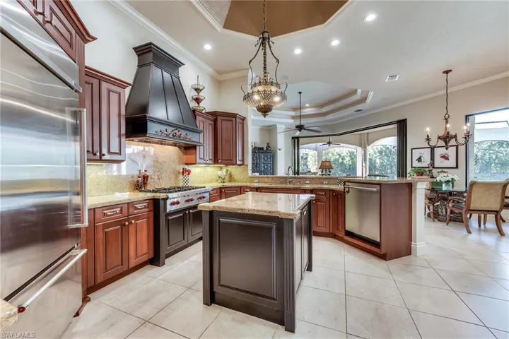 Kitchen featuring a peninsula, a sink, appliances with stainless steel finishes, a raised ceiling, and custom range hood
