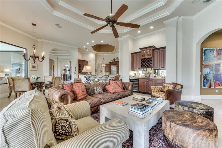 Living room featuring beverage cooler, visible vents, a raised ceiling, arched walkways, and ornamental molding