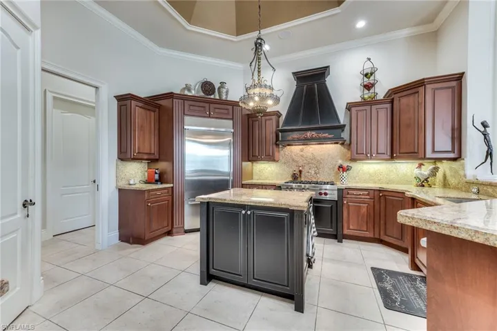 Kitchen with built in fridge, hanging light fixtures, ornamental molding, premium range hood, and range