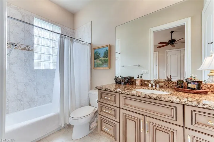 Full bath with toilet, ceiling fan, tile patterned floors, shower / bath combo with shower curtain, and vanity