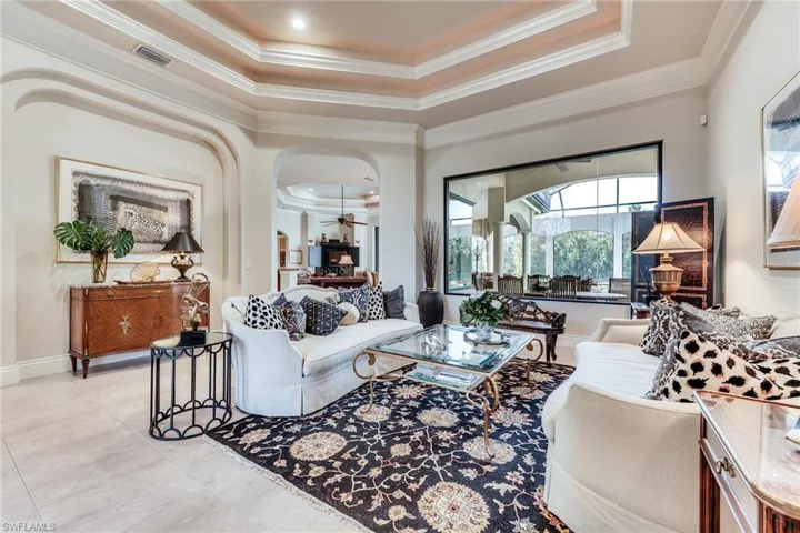 Living room featuring visible vents, arched walkways, a ceiling fan, ornamental molding, and a tray ceiling