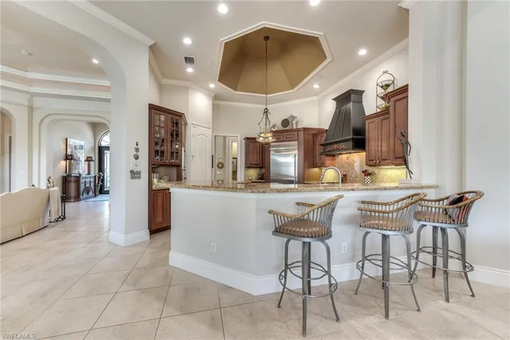 Kitchen featuring arched walkways, light stone counters, a peninsula, premium range hood, and built in fridge