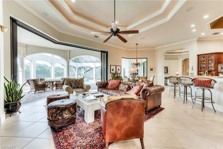 Living area with arched walkways, a tray ceiling, light tile patterned flooring, and crown molding