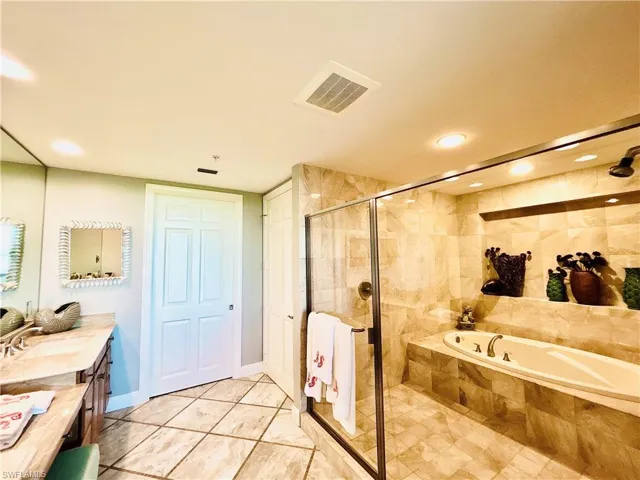 Tiled flooring, double vanity with stone countertop, built-in soaking tub, glass-enclosed shower, and recessed lighting