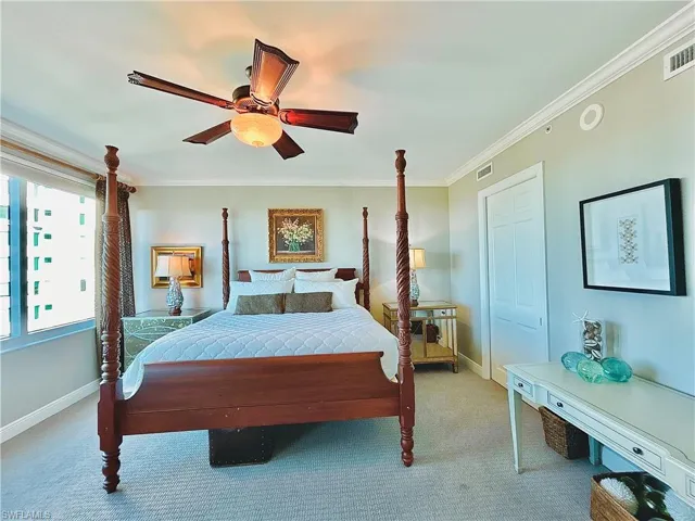 Master bedroom with four-poster wood bed frame, ceiling fan with integrated lighting, light blue wall finishes, carpeted flooring, and dual windows providing natural light
